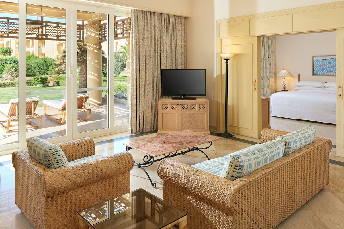 A hotel room with wicker furniture, a flat-screen TV, a bed, and a view of the garden.