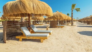 A beach with thatched umbrellas, wooden lounge chairs, and palm trees. - Sheraton Soma Bay Resort (Soma Bay)