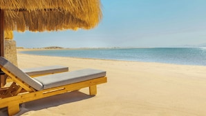 A beach with a wooden lounge chair and a thatched umbrella. - Sheraton Soma Bay Resort (Soma Bay)