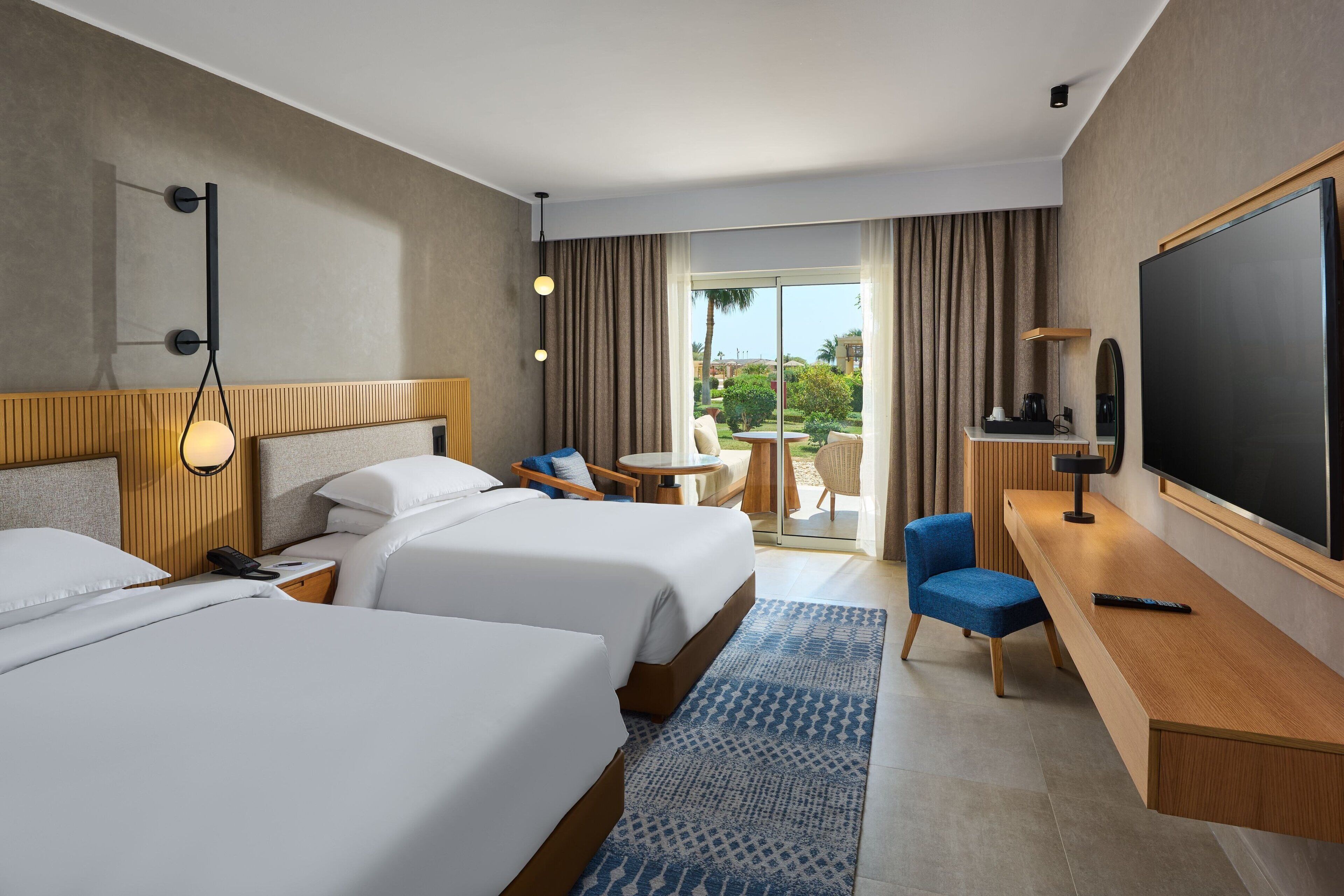 Une chambre d’hôtel avec deux lits, un bureau, une télévision et un balcon avec des meubles d’extérieur.