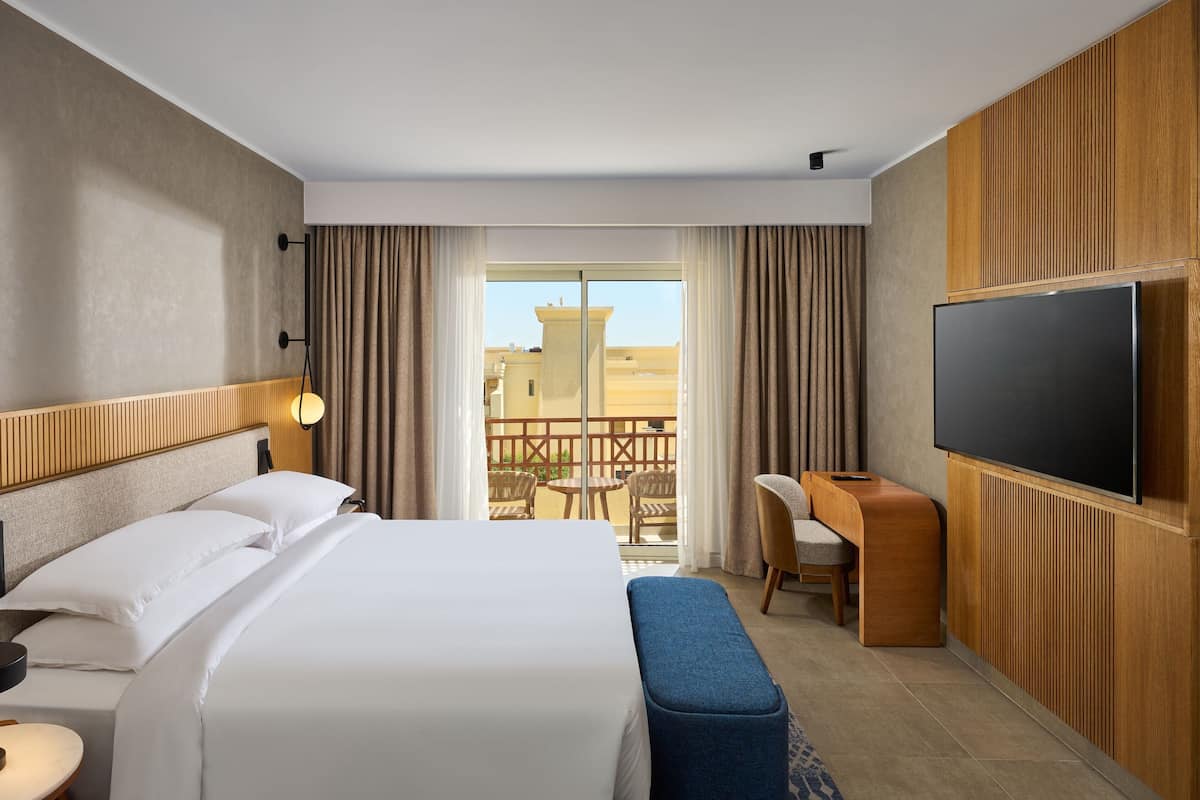 A hotel room with a large bed, a desk, a chair, and a TV.
