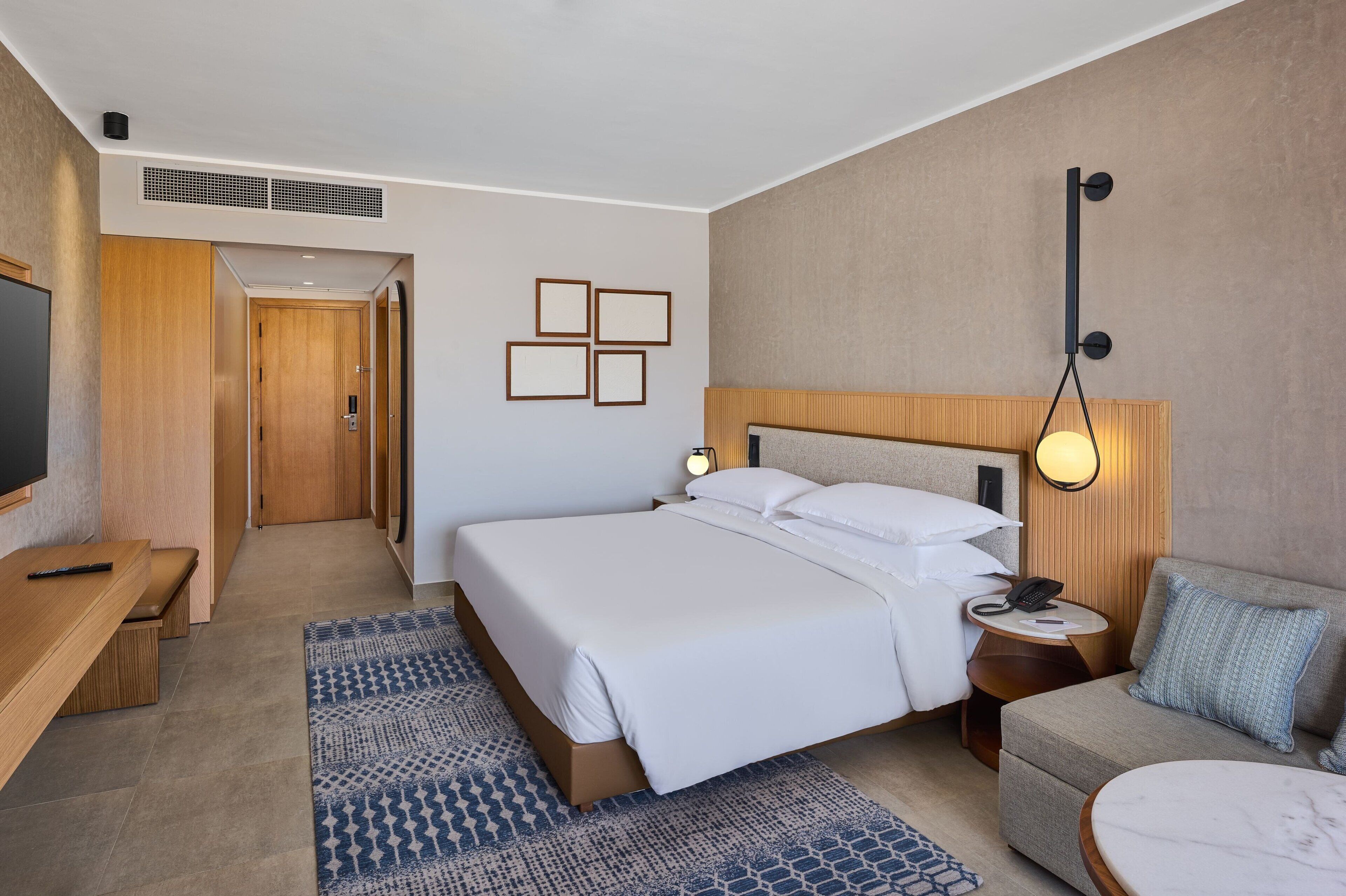 Une chambre d’hôtel avec un grand lit, des tables de chevet, un canapé, une télévision et un luminaire fixé au mur.