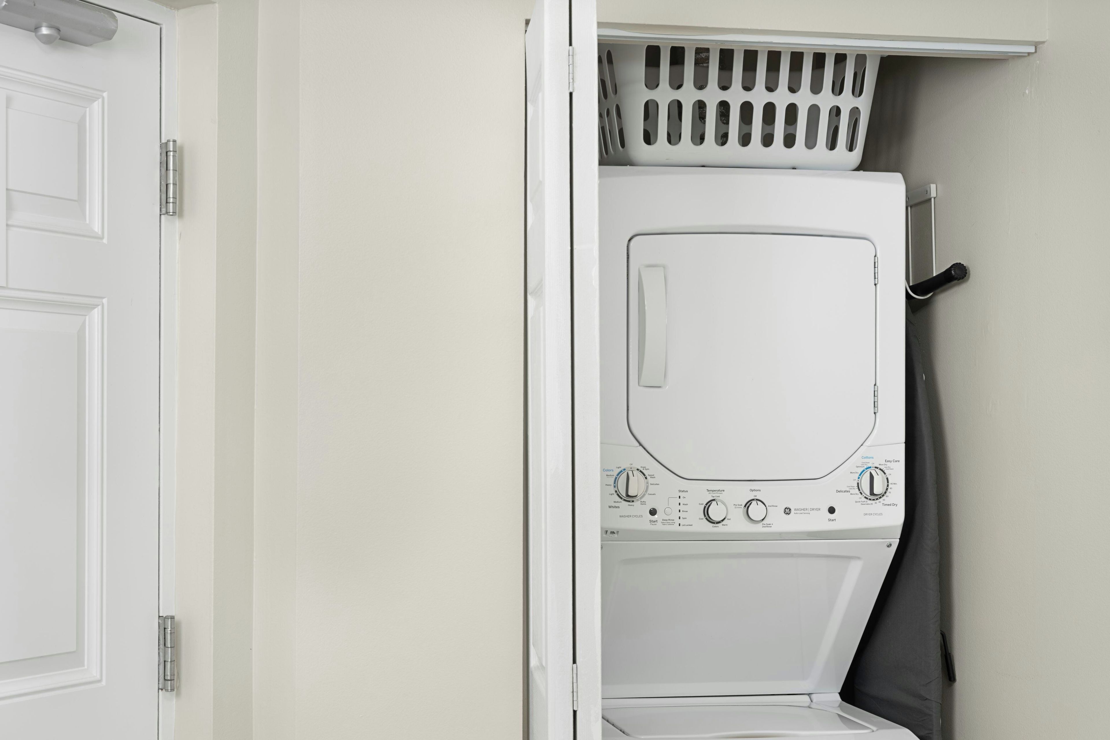 A white laundry room with a front-loading washing machine, a drying rack, and a door.
