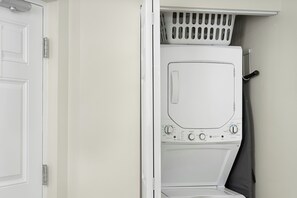 A white laundry room with a front-loading washing machine, a drying rack, and a door. - Sheraton PGA Vacation Resort, Port St. Lucie (Port Saint Lucie)