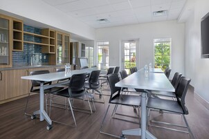 Un salón de conferencias con una larga mesa, sillas y una zona de kitchenette.