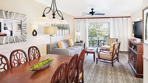 Habitación de hotel con comedor, sofá, televisión y balcón con mobiliario exterior.