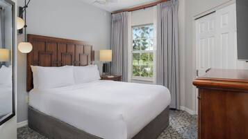 A hotel room with a large bed, a wooden headboard, two bedside lamps, a window with curtains, and a door.