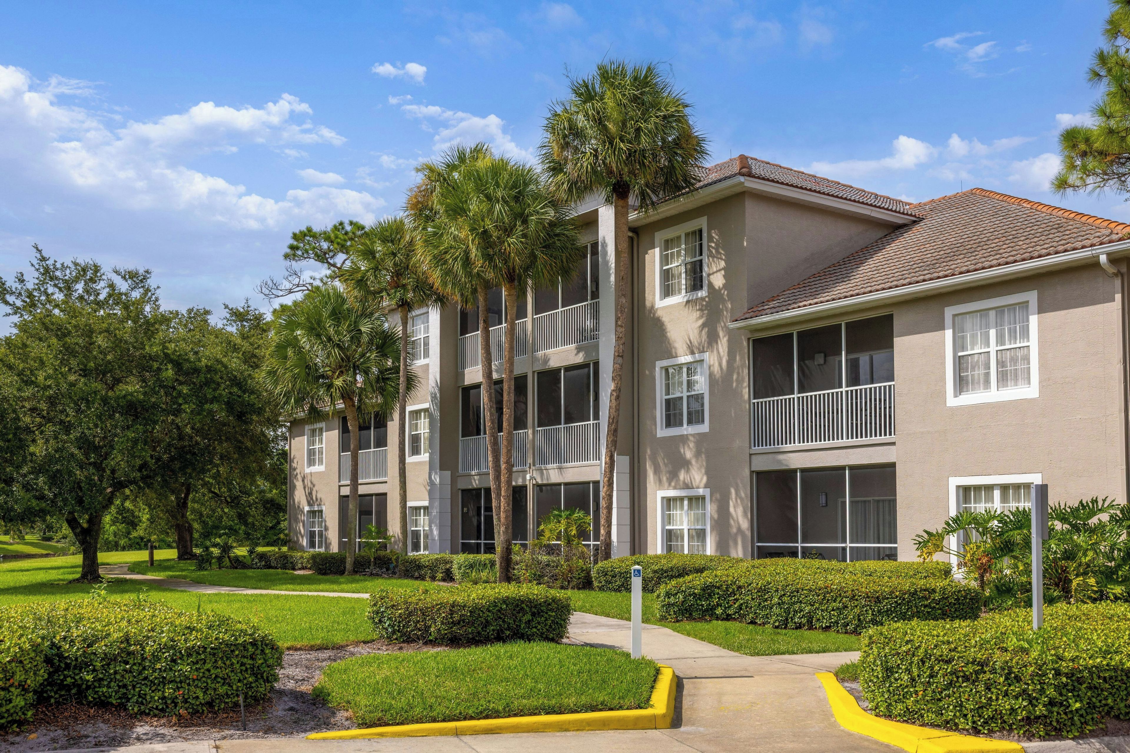 A multi-story residential building with balconies, surrounded by well-maintained landscaping and trees.