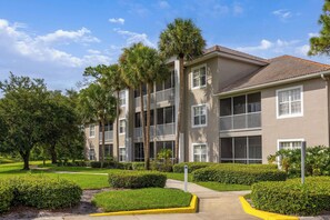 A multi-story residential building with balconies, surrounded by well-maintained landscaping and trees.