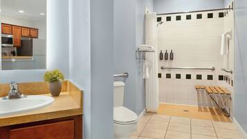 A modern bathroom with a sink, toilet, shower, and wooden bench.