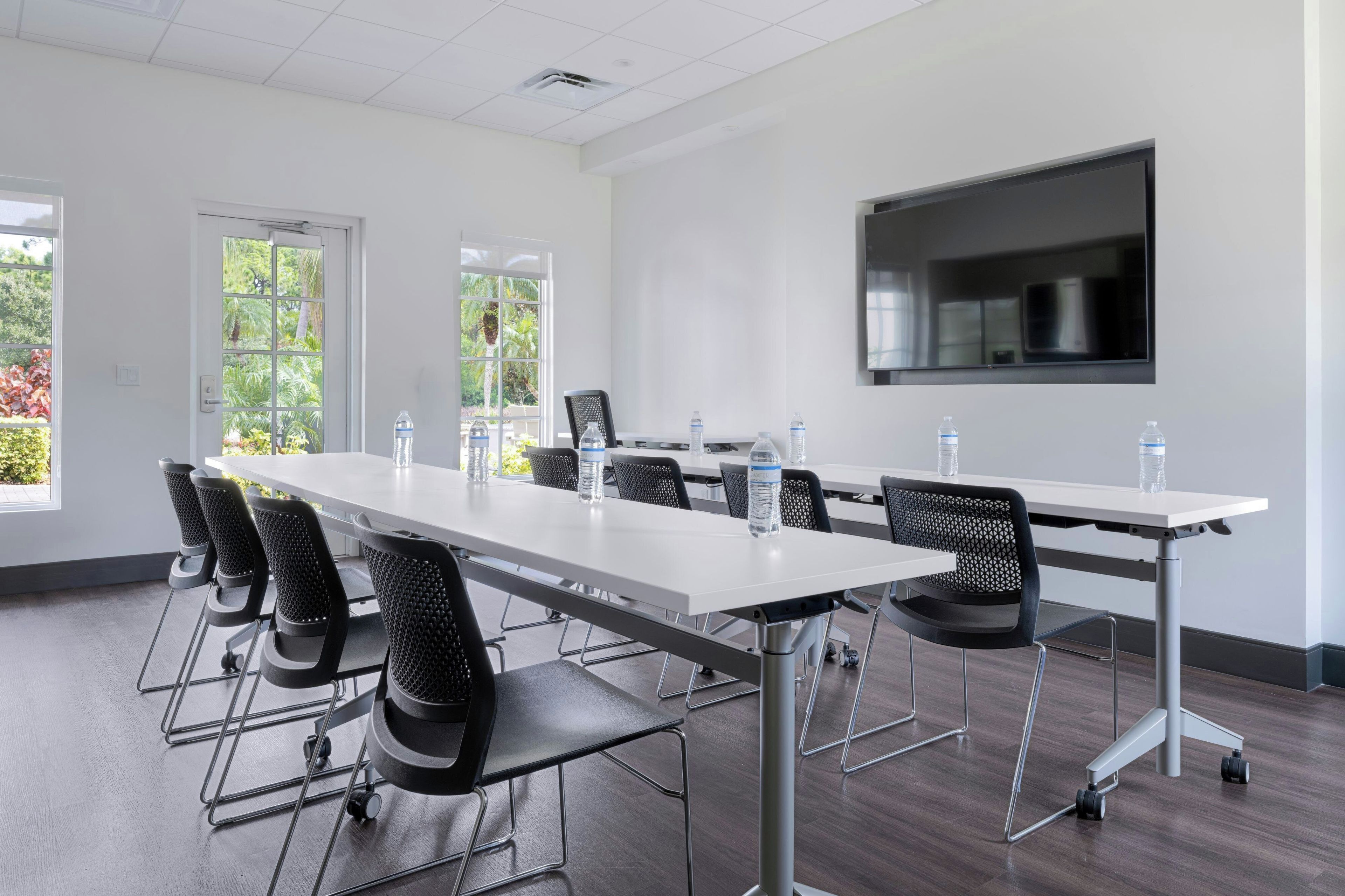 A conference room with a long table, chairs, water bottles, and a projector screen.