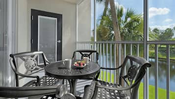 A balcony with a table and chairs, overlooking a body of water and palm trees.