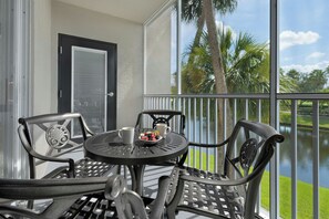 Een balkon met een tafel en stoelen, uitkijkend op een wateroppervlak en palmbomen.