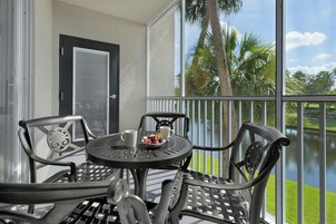 A balcony with a table and chairs, overlooking a body of water and palm trees.
