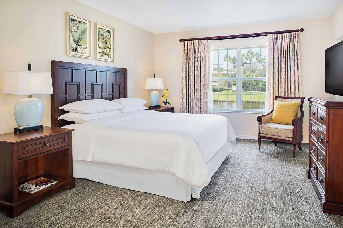Une chambre d’hôtel avec un grand lit, deux tables de chevet avec des lampes, une chaise, une commode et un téléviseur.