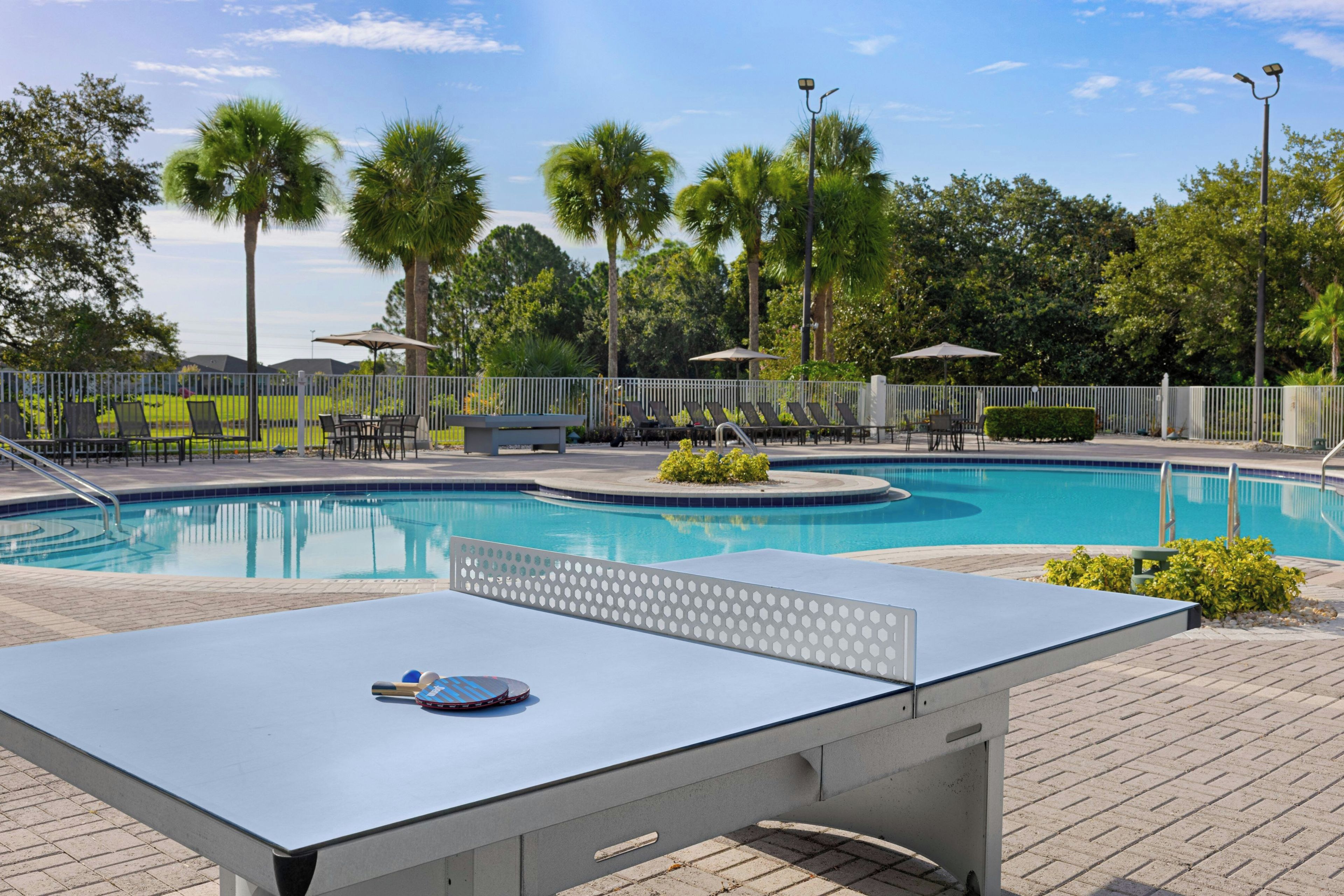 A pool area with a table tennis table, lounge chairs, and a fenced deck.