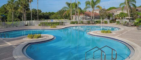 Una gran piscina al aire libre con diseño curvo, rodeada de palmeras y una valla blanca.