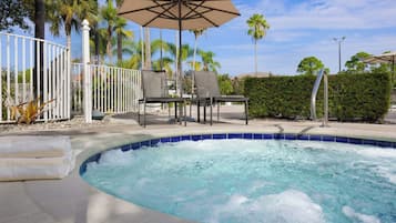 Une piscine à bord incurvé, entourée d’une clôture blanche, de palmiers et d’un espace de détente extérieur agrémenté de parasols.