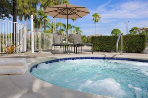 A swimming pool with a curved edge, surrounded by a white fence, palm trees, and outdoor seating with umbrellas. - Sheraton PGA Vacation Resort, Port St. Lucie (Port Saint Lucie)
