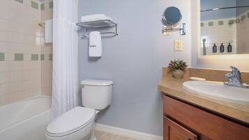 Un baño con inodoro, cortina de ducha, toallero, lavabo, espejo y artículos de aseo.