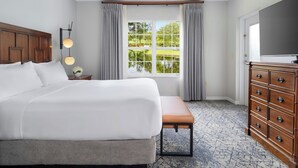 A hotel room with a large bed, a wooden dresser, a bench, a nightstand, a lamp, and a window with a view of greenery. - Sheraton PGA Vacation Resort, Port St. Lucie (Port Saint Lucie)