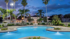 A swimming pool with a surrounding deck, palm trees, and a building with a tiled roof in the background. - Sheraton PGA Vacation Resort, Port St. Lucie (Port Saint Lucie)