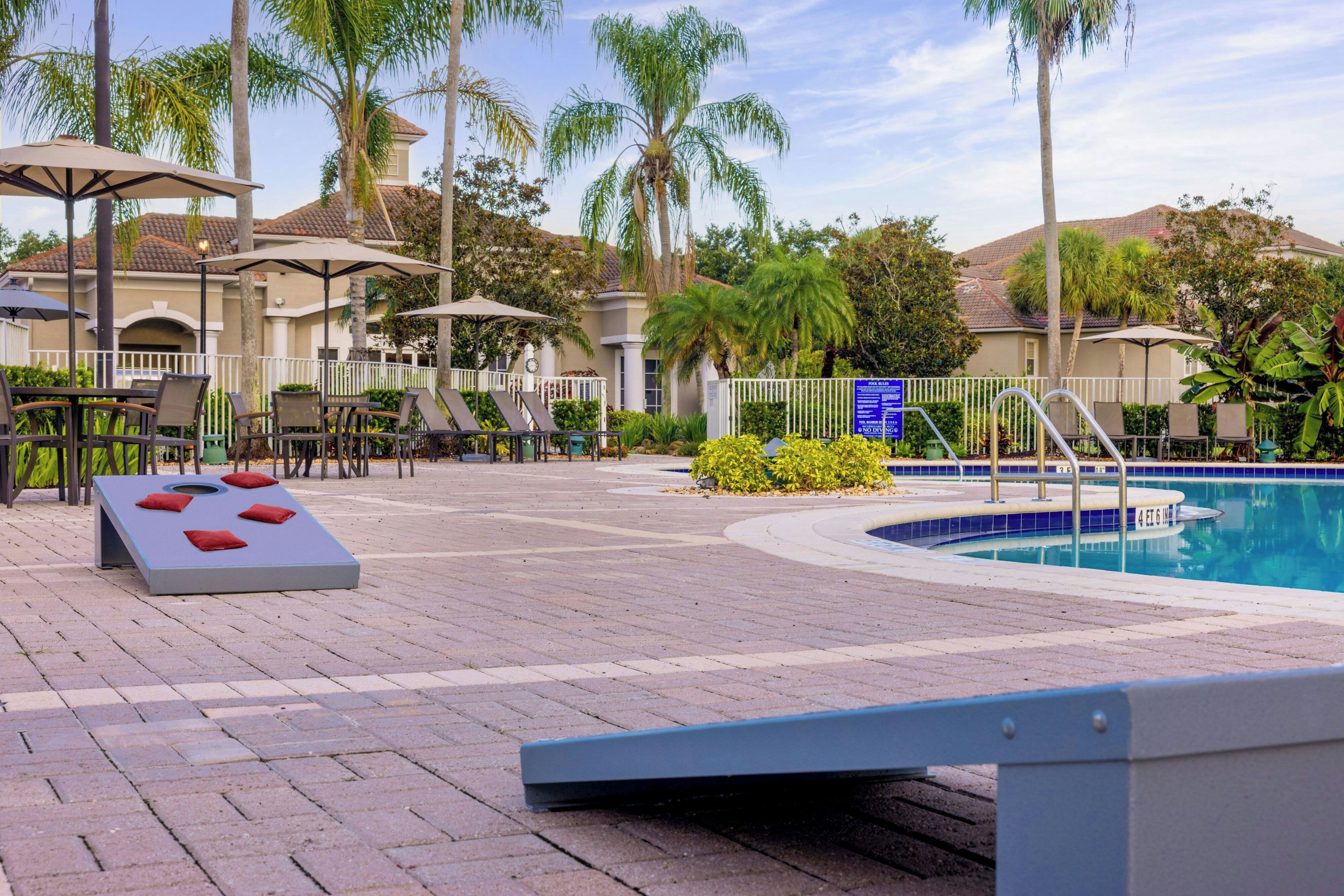 Un área de piscina con sillas de descanso, una tumbona y una piscina con borde de azulejos azules.