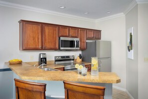 A kitchen with wooden cabinets, a stainless steel refrigerator, a microwave, an oven, and a coffee maker. There is a bar area with two chairs and a pitcher of lemonade. - Sheraton PGA Vacation Resort, Port St. Lucie (Port Saint Lucie)
