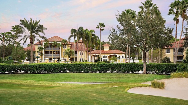 A golf course with a well-maintained lawn, a sand bunker, and a row of multi-story buildings with balconies and large windows. - Sheraton PGA Vacation Resort, Port St. Lucie (Port Saint Lucie)