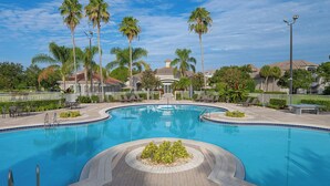 A large outdoor swimming pool with a central island, surrounded by palm trees and lounge chairs, with a building in the background. - Sheraton PGA Vacation Resort, Port St. Lucie (Port Saint Lucie)