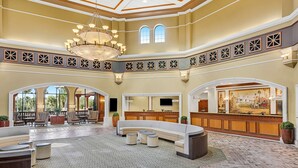 A spacious lobby with a high ceiling, a central chandelier, a reception desk, and a large seating area.