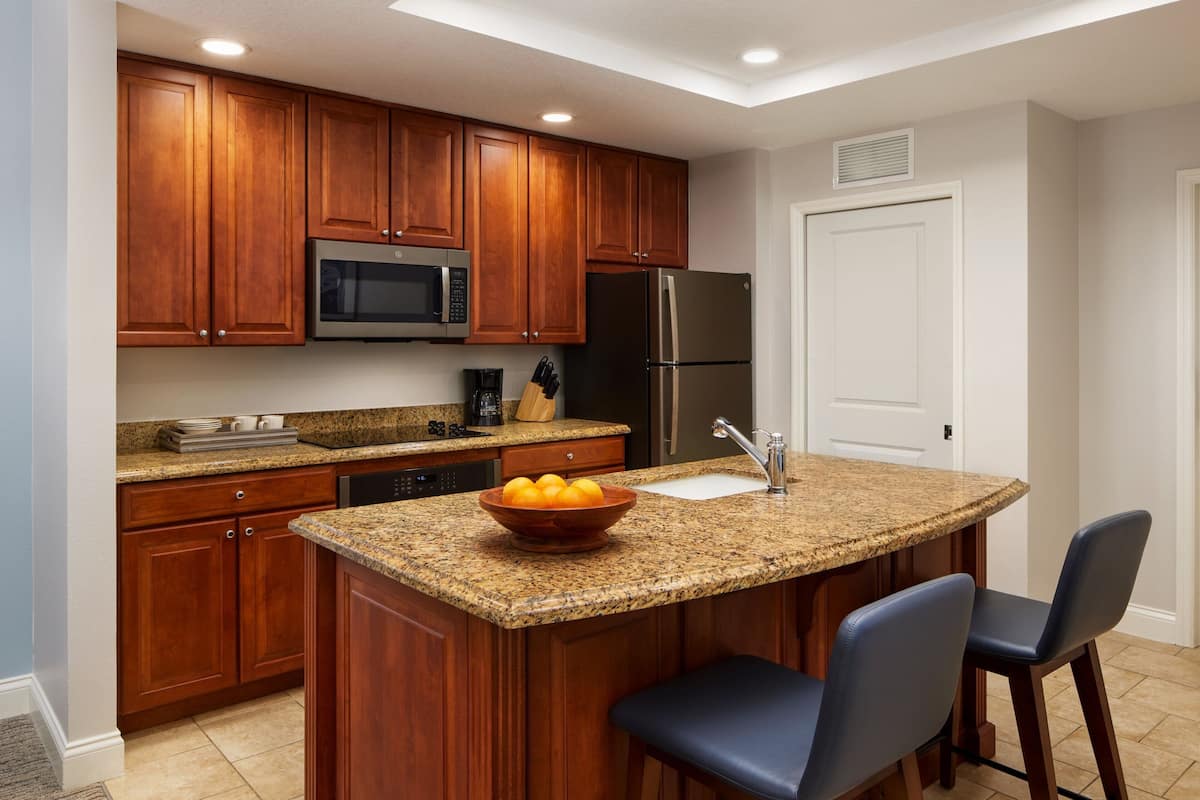 A kitchen with wooden cabinets, a granite countertop, a stainless steel refrigerator, and a microwave.