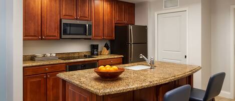 A kitchen with wooden cabinets, a granite countertop, a stainless steel refrigerator, and a microwave.