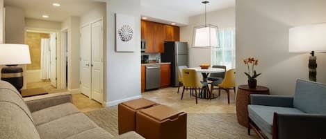 A modern living room with a sofa, ottomans, a dining area with a table and chairs, and a kitchen with appliances.