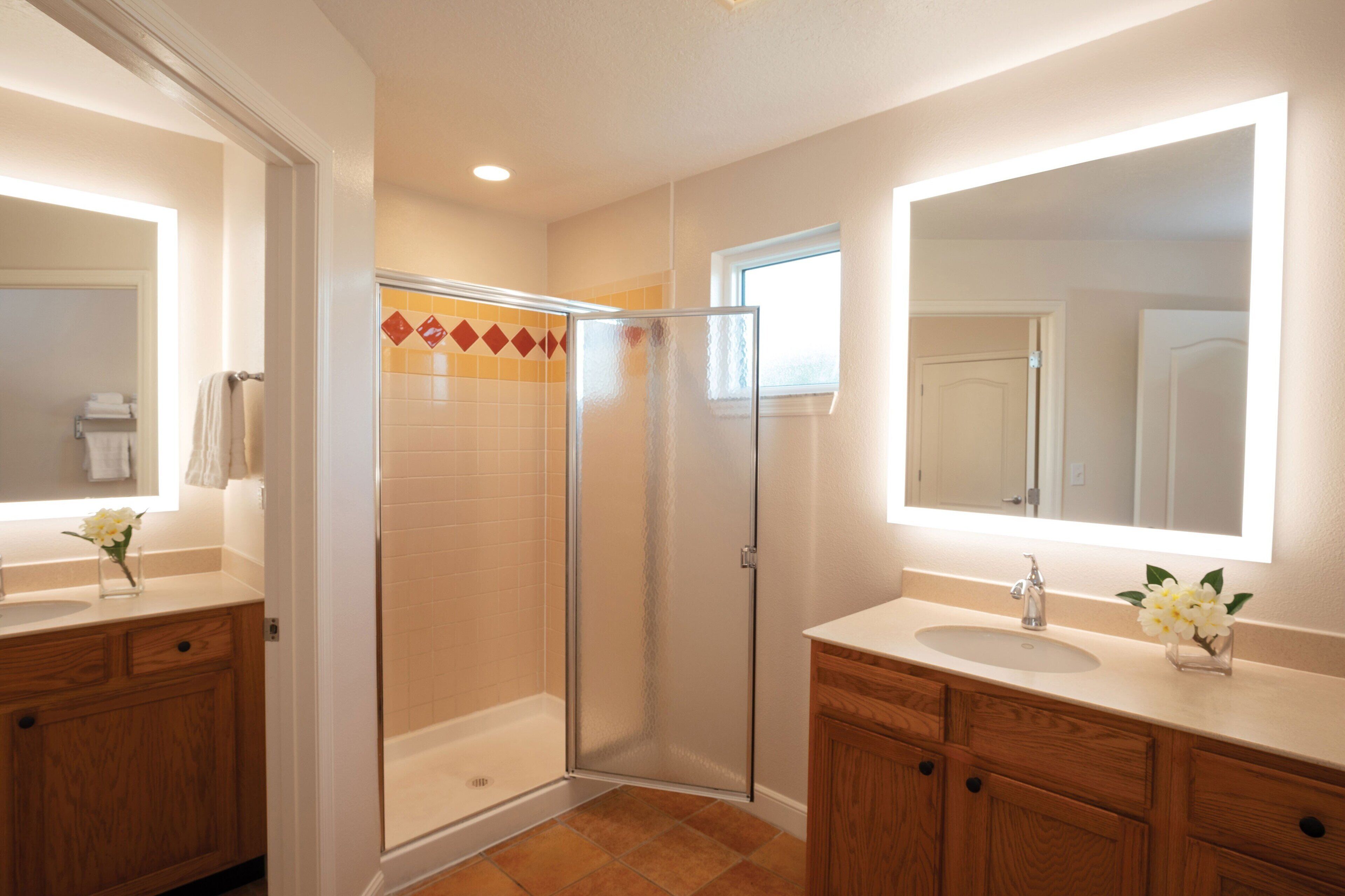 A modern bathroom with two sinks, wooden cabinets, a glass shower enclosure, and a large mirror.