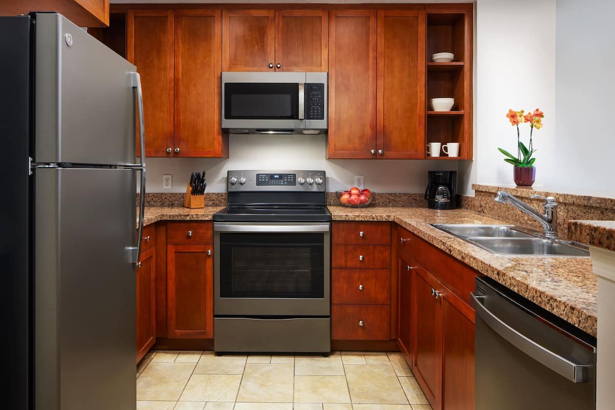 A modern kitchen with stainless steel appliances, wooden cabinets, granite countertops, and a built-in oven.