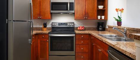 A modern kitchen with stainless steel appliances, wooden cabinets, granite countertops, and a built-in oven.