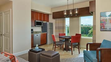 A modern kitchen with built-in appliances, a dining area with a round table and chairs, and a living room with a sofa and ottoman.