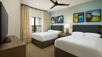 A hotel room with two beds, a TV, a ceiling fan, and artwork on the walls.