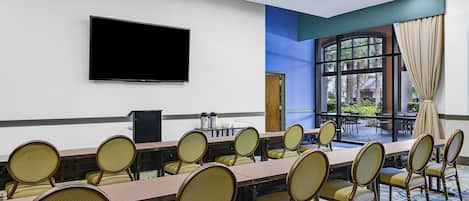 Un salón de conferencias con una mesa larga, sillas, un televisor de pantalla plana y un ventanal con vistas al exterior.