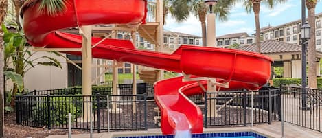 A pool area with a red water slide and a pool.
