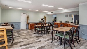 Un comedor con mesas y sillas de madera, una cocina con electrodomésticos, y una puerta que da a otra habitación.