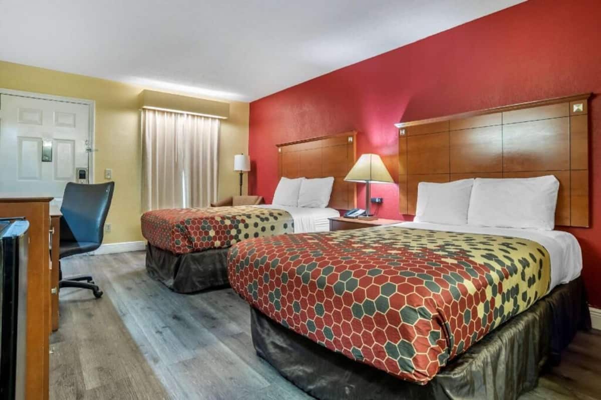 Ein Hotelzimmer mit zwei Betten, einem Schreibtisch, einem Stuhl und einem Vorhangfenster.