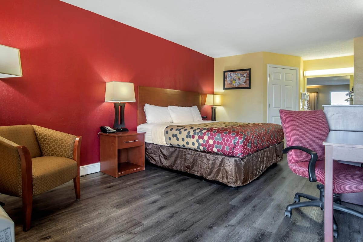 Ein Hotelzimmer mit einem Bett, einem Schreibtisch, einem Sessel, einem Nachttisch und einer Lampe.