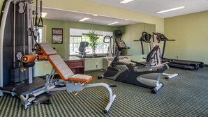 Un gimnasio con máquinas de cardio, una banca de pesas y un espejo grande.