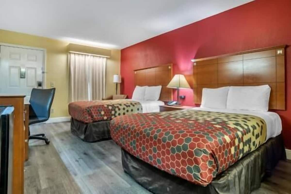 Ein Hotelzimmer mit zwei Betten, einem Schreibtisch, einem Stuhl und einem Fenster mit Vorhängen.
