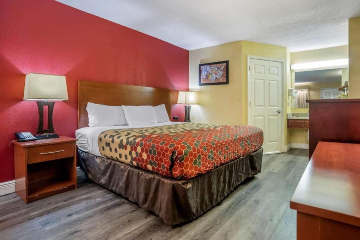 Ein Hotelzimmer mit Bett, Nachttischen, Schreibtisch, Stuhl und einem im Hintergrund sichtbaren Badezimmer.