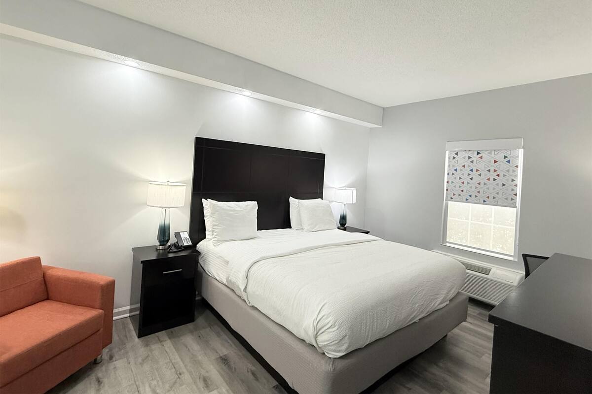 A modern hotel room with a large bed, bedside lamps, a small desk, and a chair.