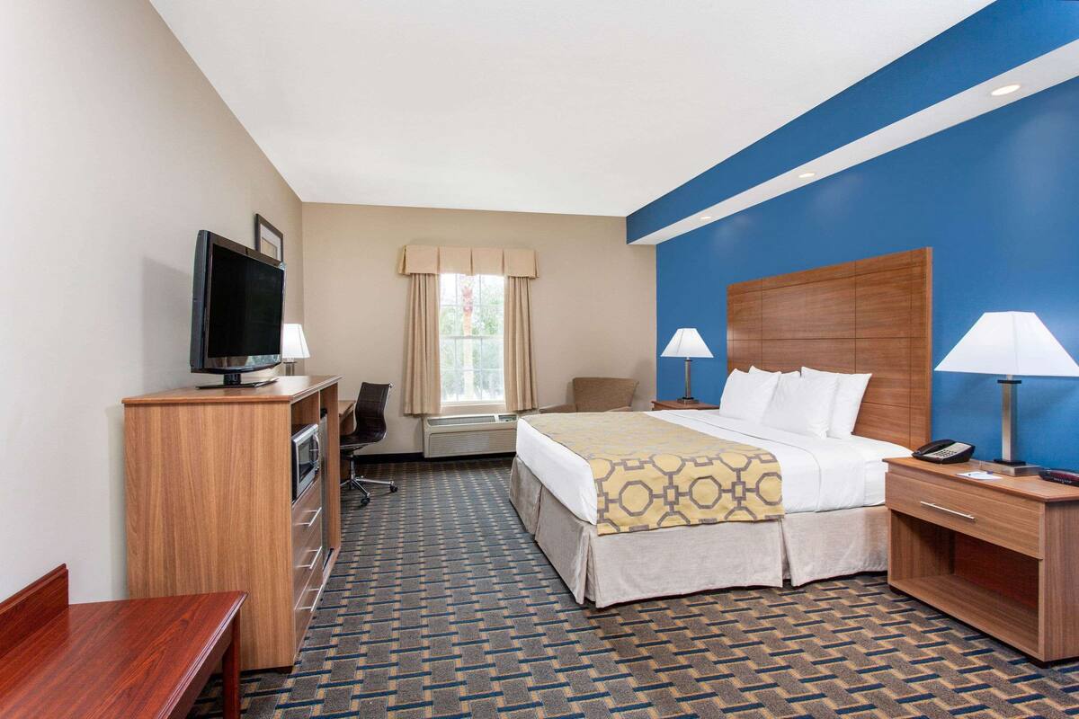 Une chambre d’hôtel comprenant un lit, des tables de chevet, un bureau, une chaise, un téléviseur et une fenêtre avec des rideaux.