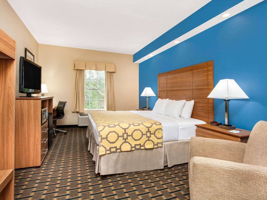 A hotel room with a bed, two bedside lamps, a desk with a TV, a chair, and a patterned carpet.